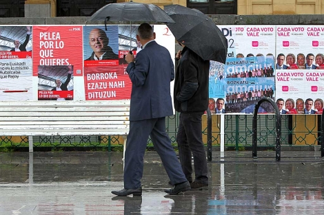 Dos hombres conp araguas observan los carteles electorales frente al Ayuntamiento de San Sebastián. | Juan Herrero | Efe