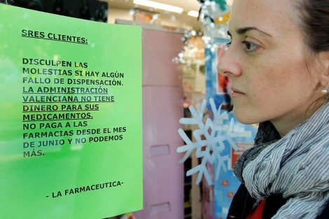 Una joven lee un cartel en una farmacia donde se quejan por el retraso en los pagos | Efe