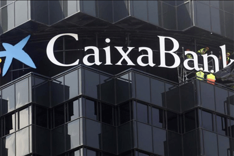 Operarios cambian un cartel en la sede de Caixabank. | EM
