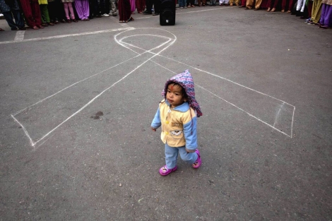 Una niña nepalí camina frente a un lazo contra el sida. | Efe