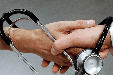 Una mano de un paciente entrelazada por un fonendoscopio de un médico. | El Mundo